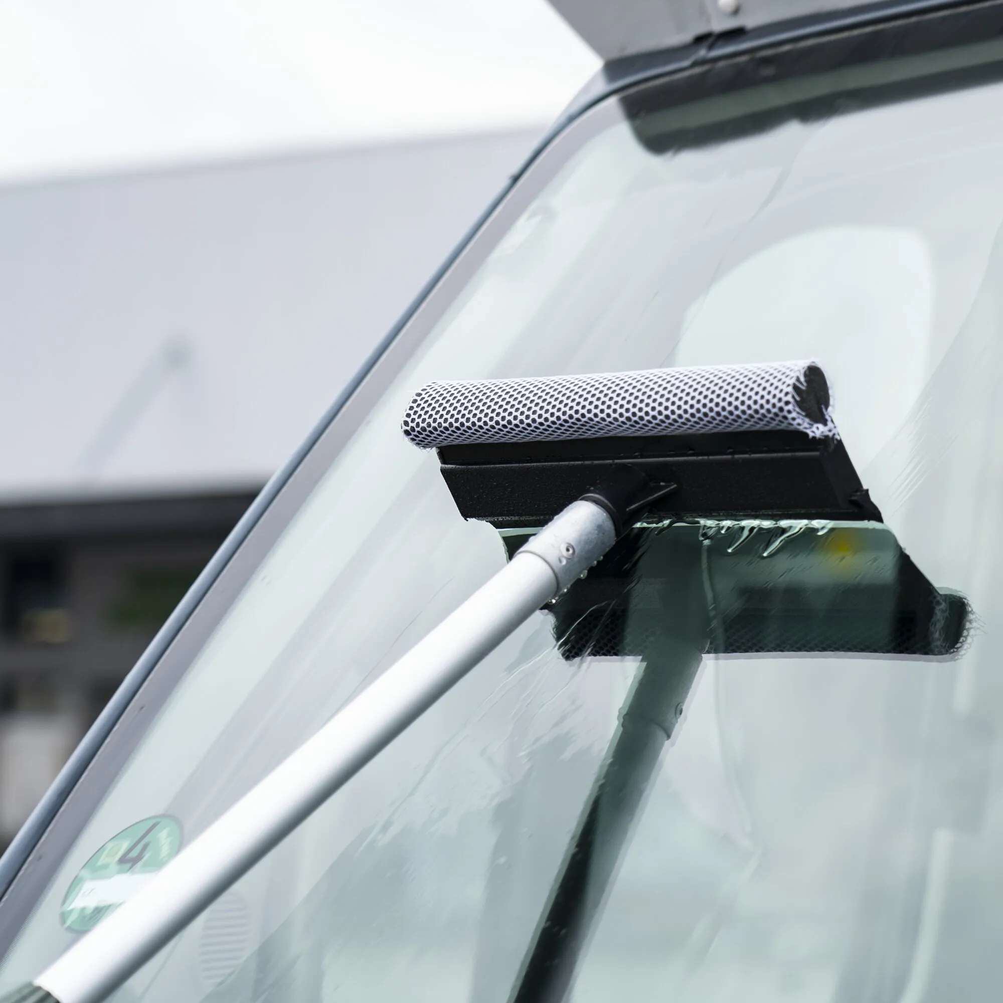 Scheibenabzieher mit schwarzem Fliegenentferner beim Reinigen einer nassen Autoscheibe