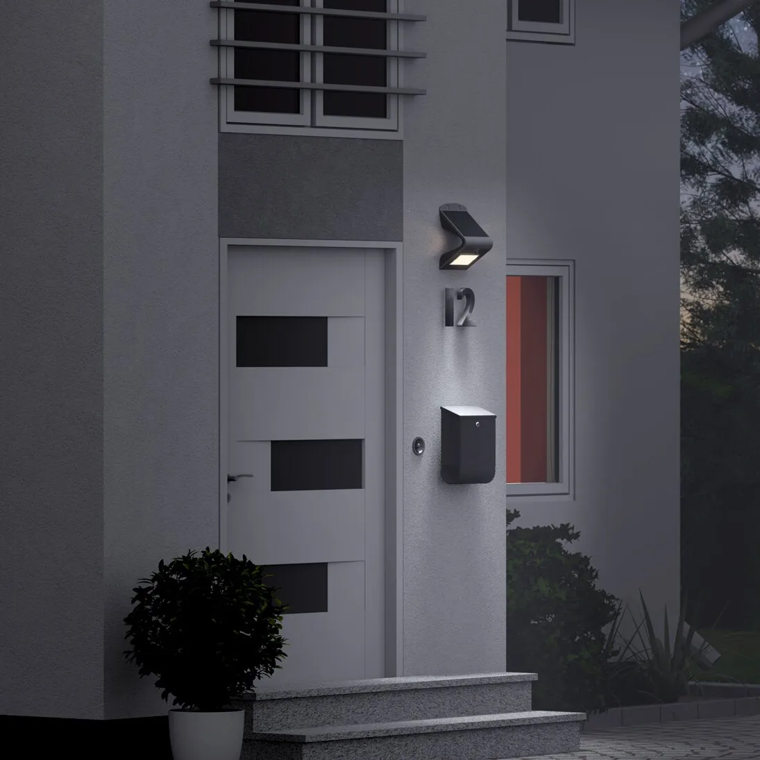 Schwarze LED-Solar-Wandleuchte mit Bewegungsmelder an der Haustür, die Wand über dem Briefkasten nahe der Hausnummer 12 ausleuchtet