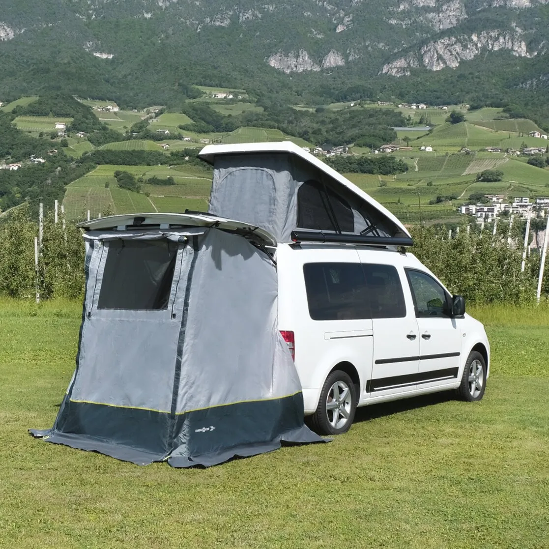 Graues Heckzelt Pilote Caddy 4 an einem weißen Hochdachkombi auf einer Wiese vor einer Berglandschaft