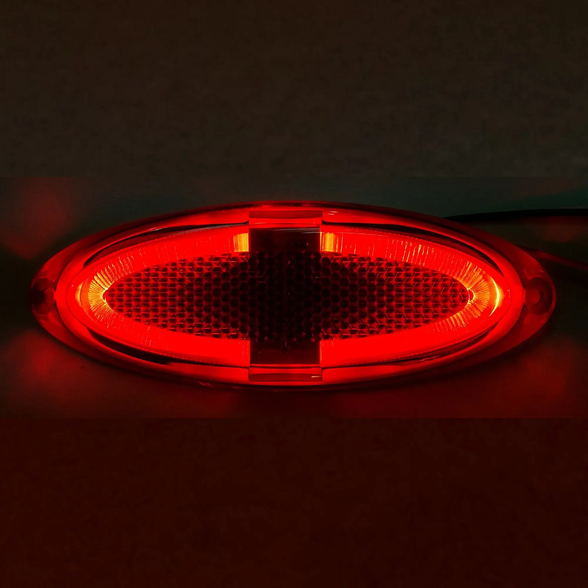 Rote ovale Markierungsleuchte mit rotem Leuchtmittel, Linse mit hexagonaler Struktur, dunkler Hintergrund