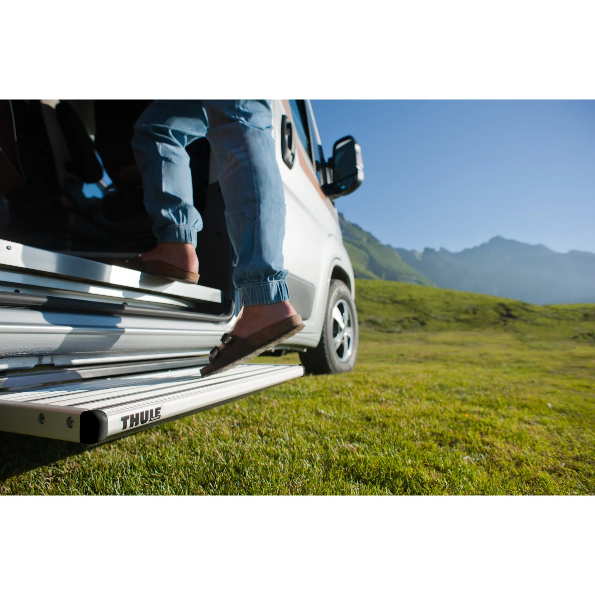 Ausgefahrene silberne Thule Single Step compact 12V 500 am Wohnmobil, während eine Person auf die Trittstufe steigt, vor Berglandschaft