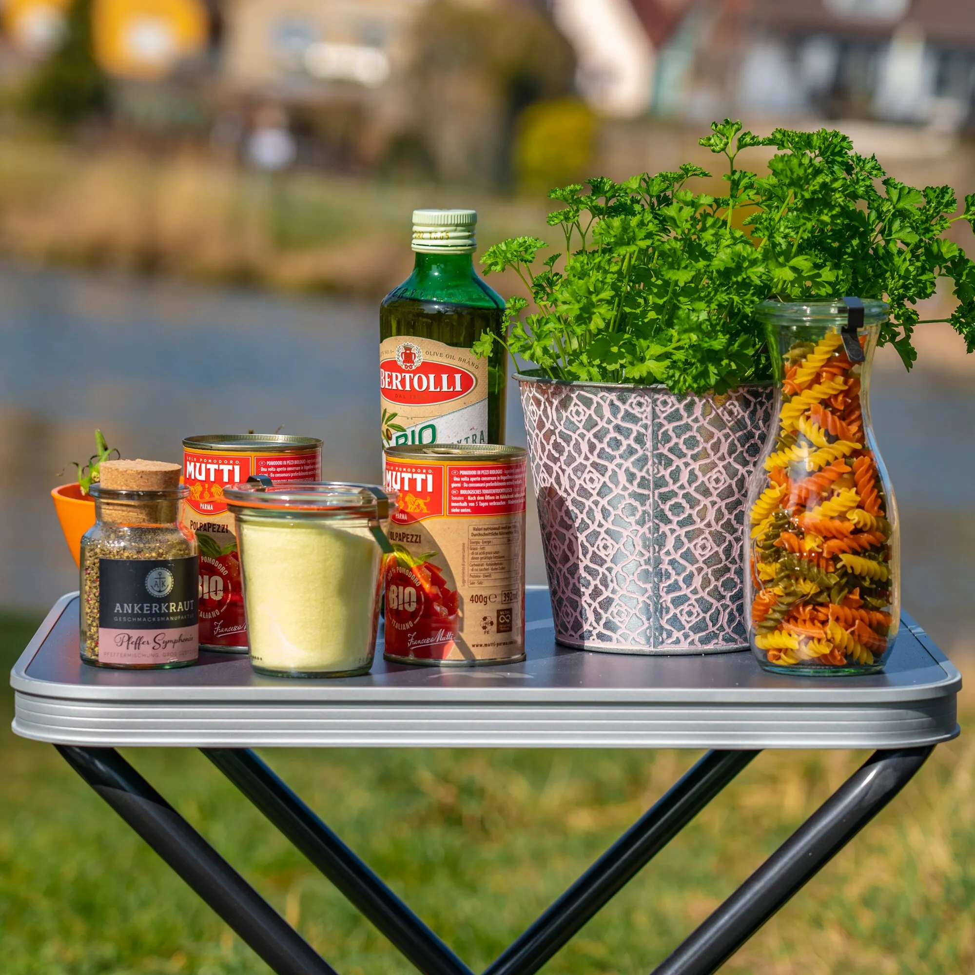 Hockerplatte HighQ als silbergraue, abgerundete Platte auf schwarzen Klappbeinen mit Kräutern, Gewürzen, Öl, Pasta und Konserven als Ablage