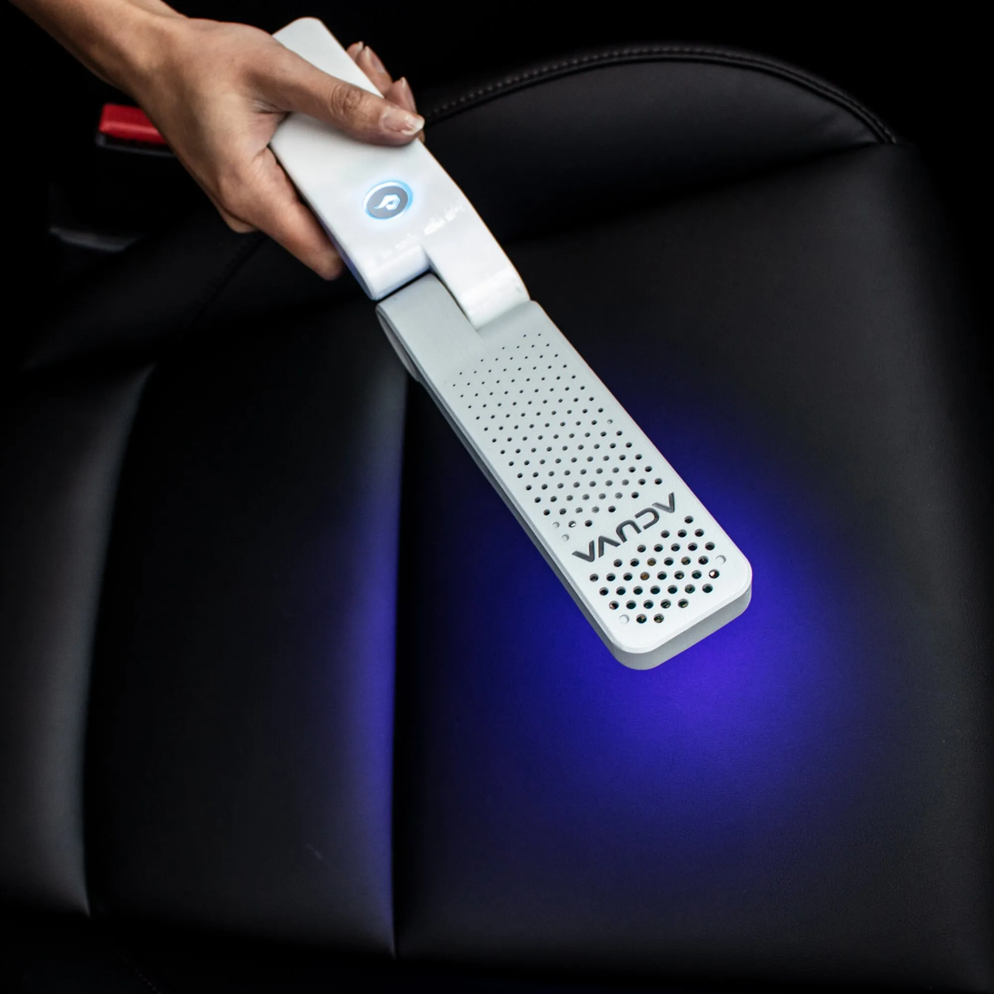 Weiße Acuva™ Solarix Oberflächen-Desinfektion wird von einer Hand über einen schwarzen Autositz geführt; blaues UV-Licht ist sichtbar