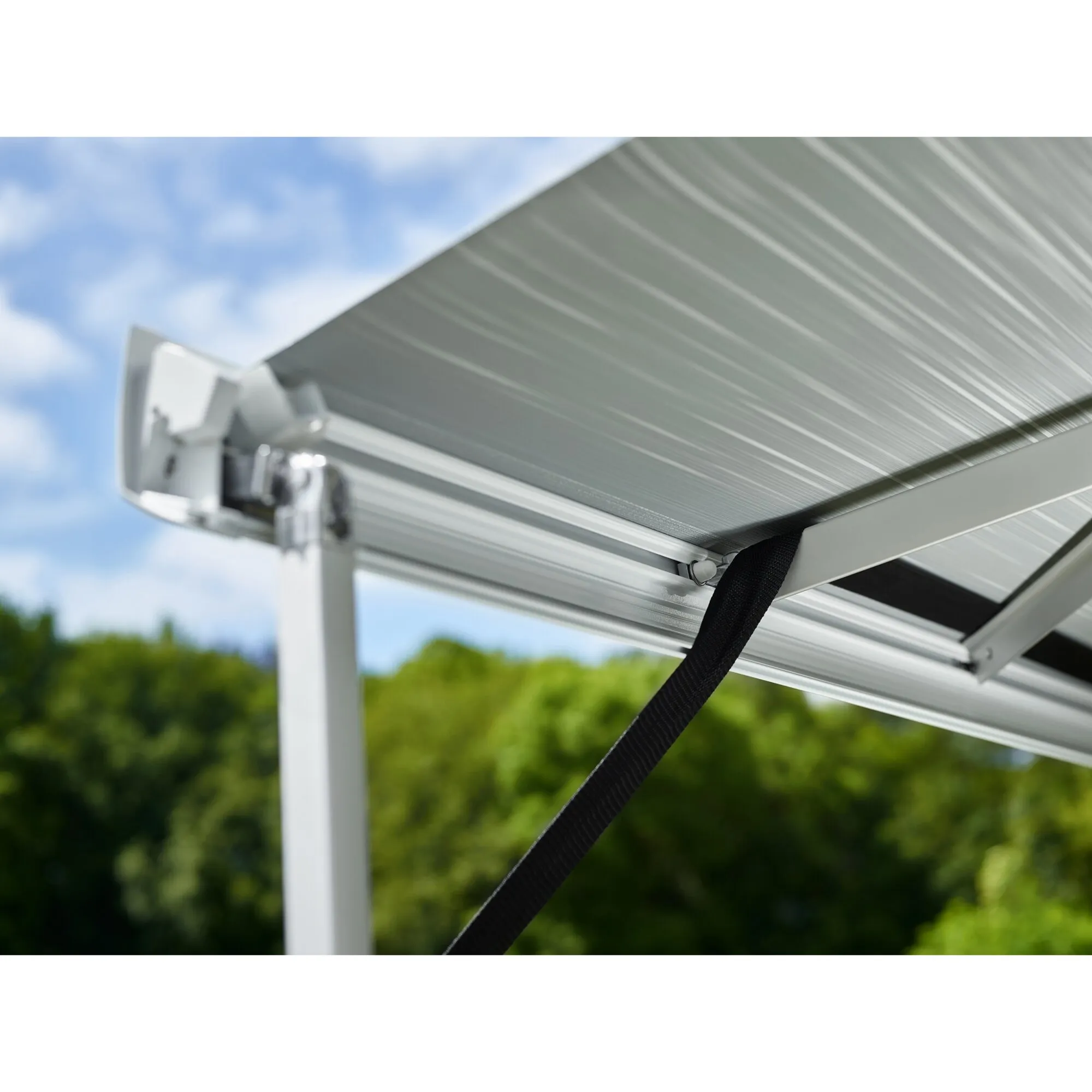 Detailaufnahme einer silbernen Thule-Markise mit schwarzem Spannband des Hold Down Kits am weißen Aluminiumgestell im Freien