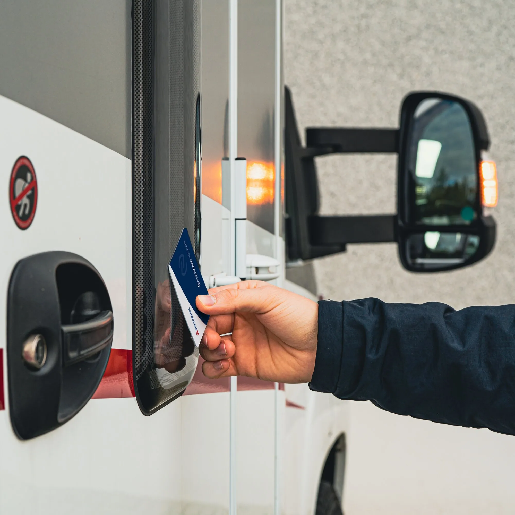 Hand hält eine blaue NFC-Transponderkarte an das Lesegerät eines Fahrzeugs zur kontaktlosen Zugangskontrolle