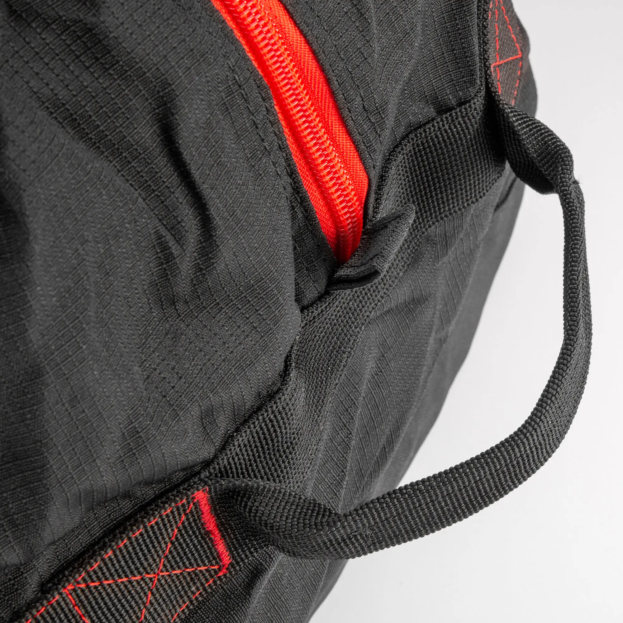 Nahaufnahme einer schwarzen Reisetasche mit rotem Reißverschluss, roter Stichnaht und gewebtem Trageband, Textur des Materials ist deutlich zu sehen