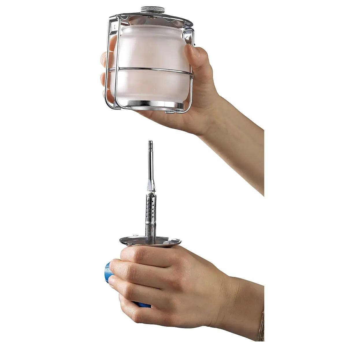 Kompakte Gaslampe mit verchromtem Rahmen, Glasbehälter und Schutzgitter; eine Hand hält das Gehäuse, die andere den Brennerstutzen