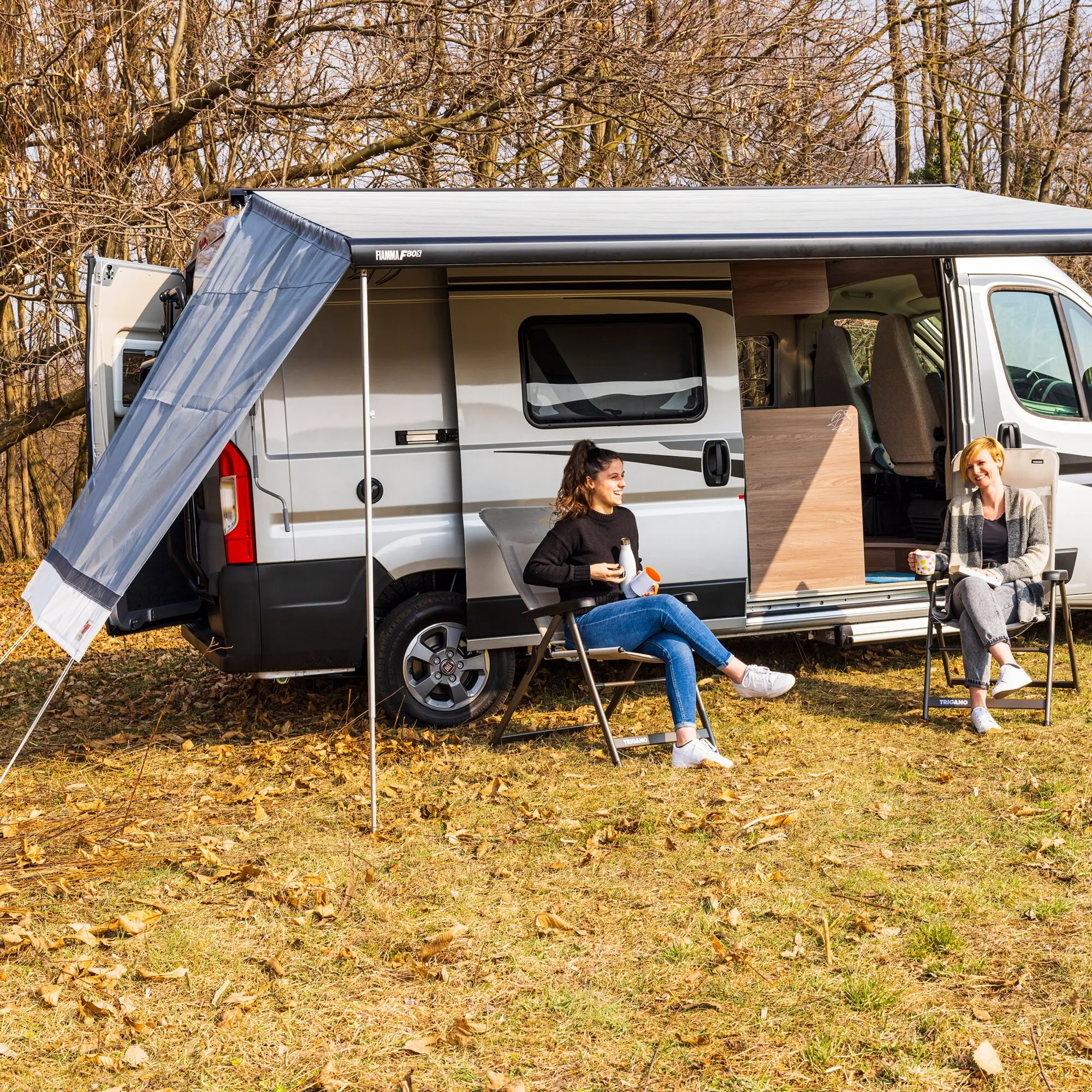 Sun View Side Seitenwand 230 cm am Wohnmobil mit Markise, grauer Stoff, seitlich geöffnet, zwei Personen sitzen in Klappstühlen vor dem Wagen