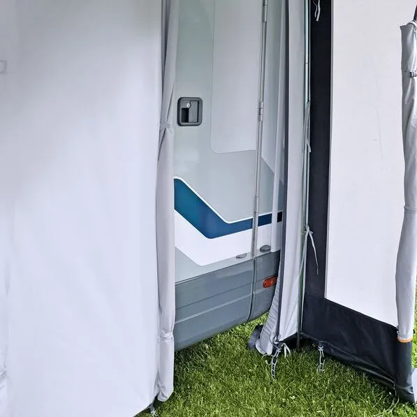 Detailansicht des Ganzjahresteilzelts Garmisch am Wohnwagen mit geöffnetem Eingang, Seitenwand und Abspannleinen auf Gras