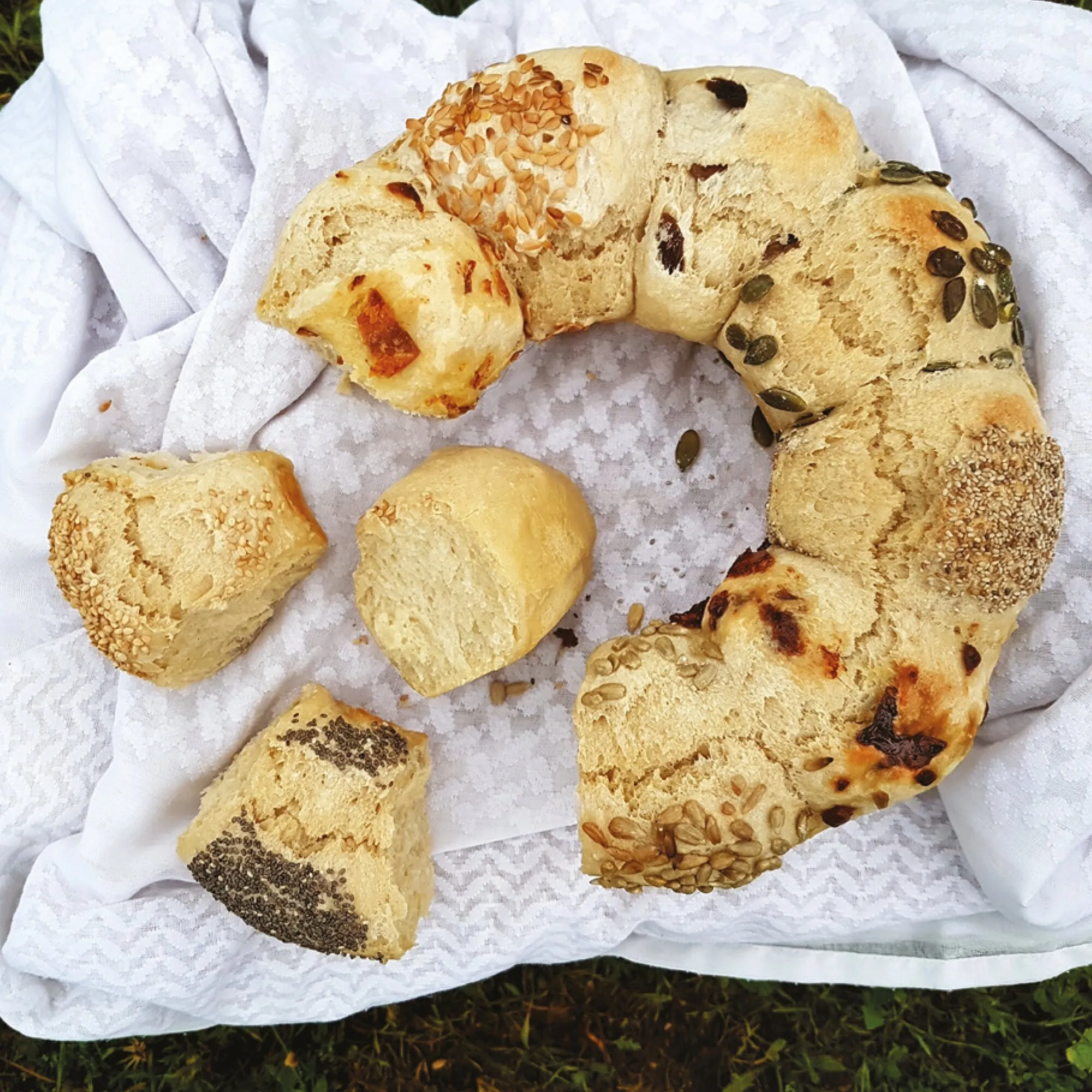Verschiedene goldbraune Brote und Brötchen mit Sonnenblumen-, Kürbis-, Sesam- und Chiasamen auf einem weißen Tuch