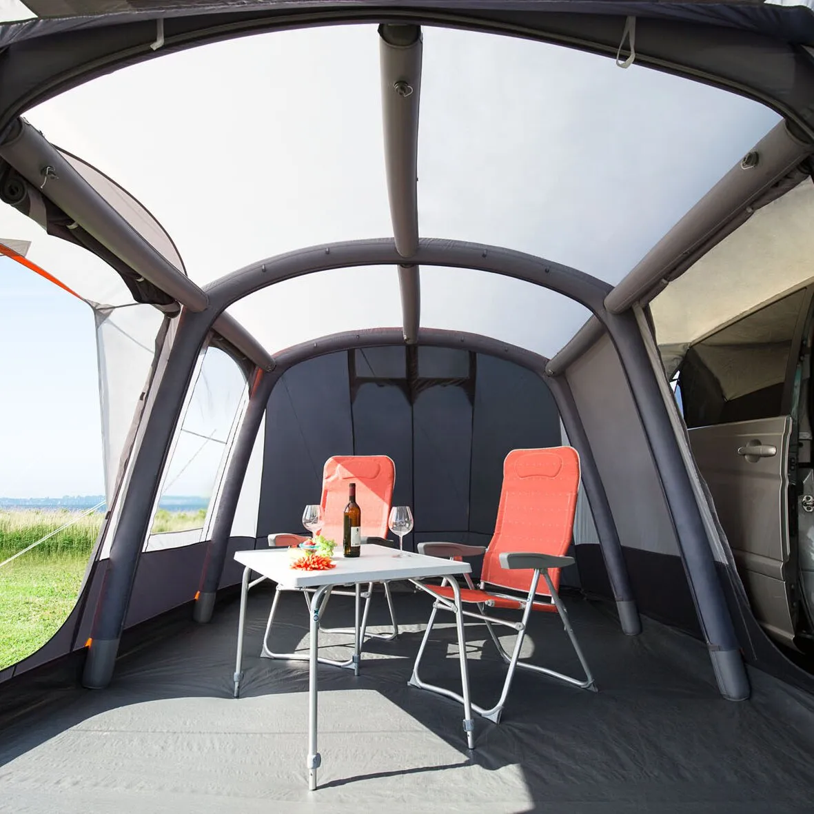 Innenansicht des Busvorzelts Pegasus Air mit aufblasbaren Luftschläuchen, Tisch und zwei roten Campingstühlen am geöffneten Campervan