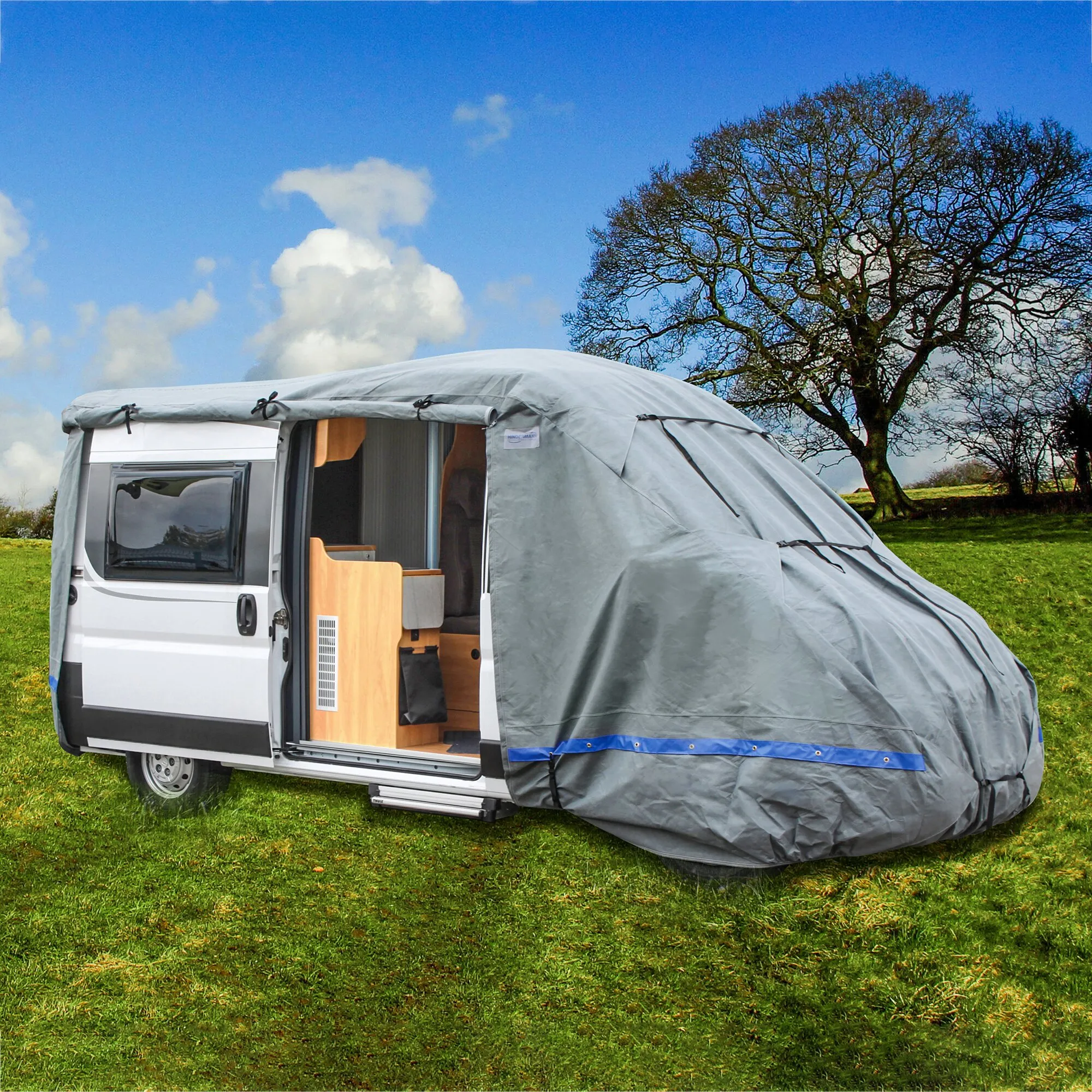 Graue Kastenwagen-Schutzhülle Wintertime für 610 cm langen Camper, mit blauen Befestigungsriemen und geöffneter Seitentür auf einer Wiese