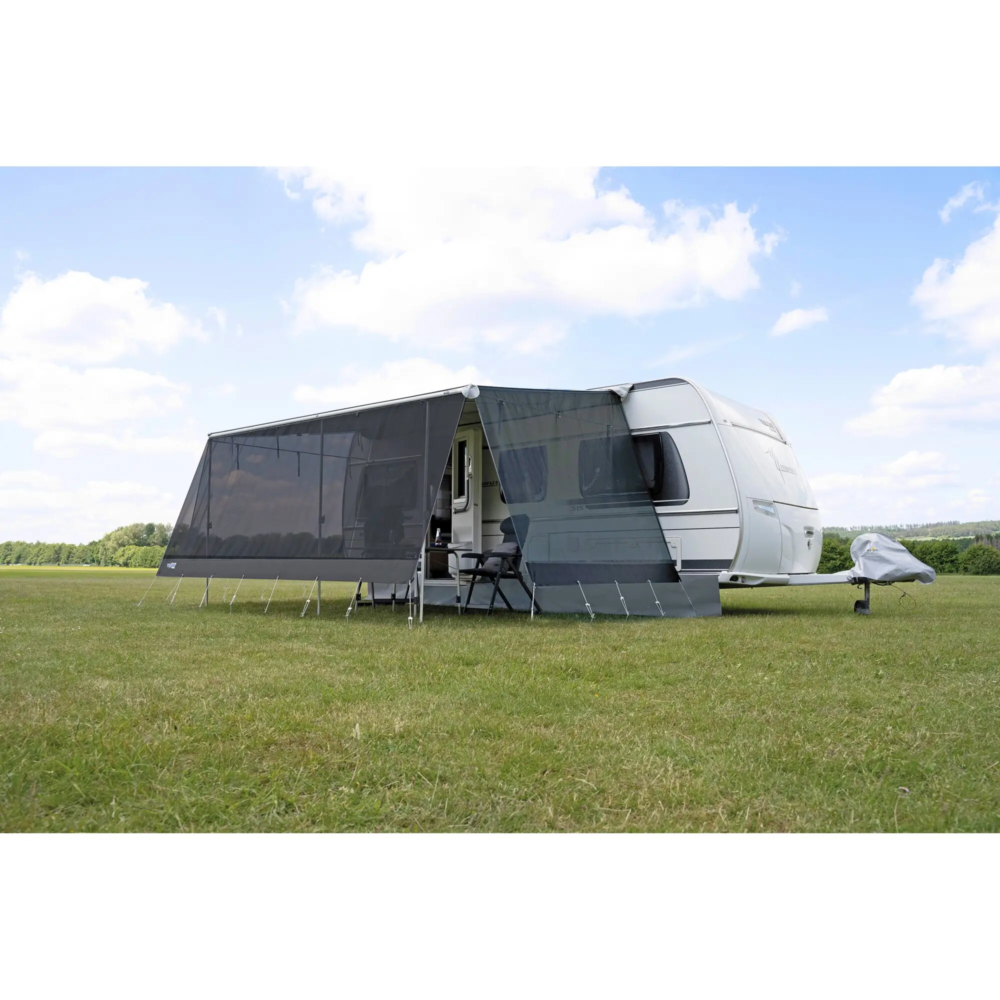 Vorderwand BLOXX Screen für Rolli Plus Größe 08b am Wohnwagen, dunkle Frontfläche mit Stützbeinen im Gras und blauem Himmel