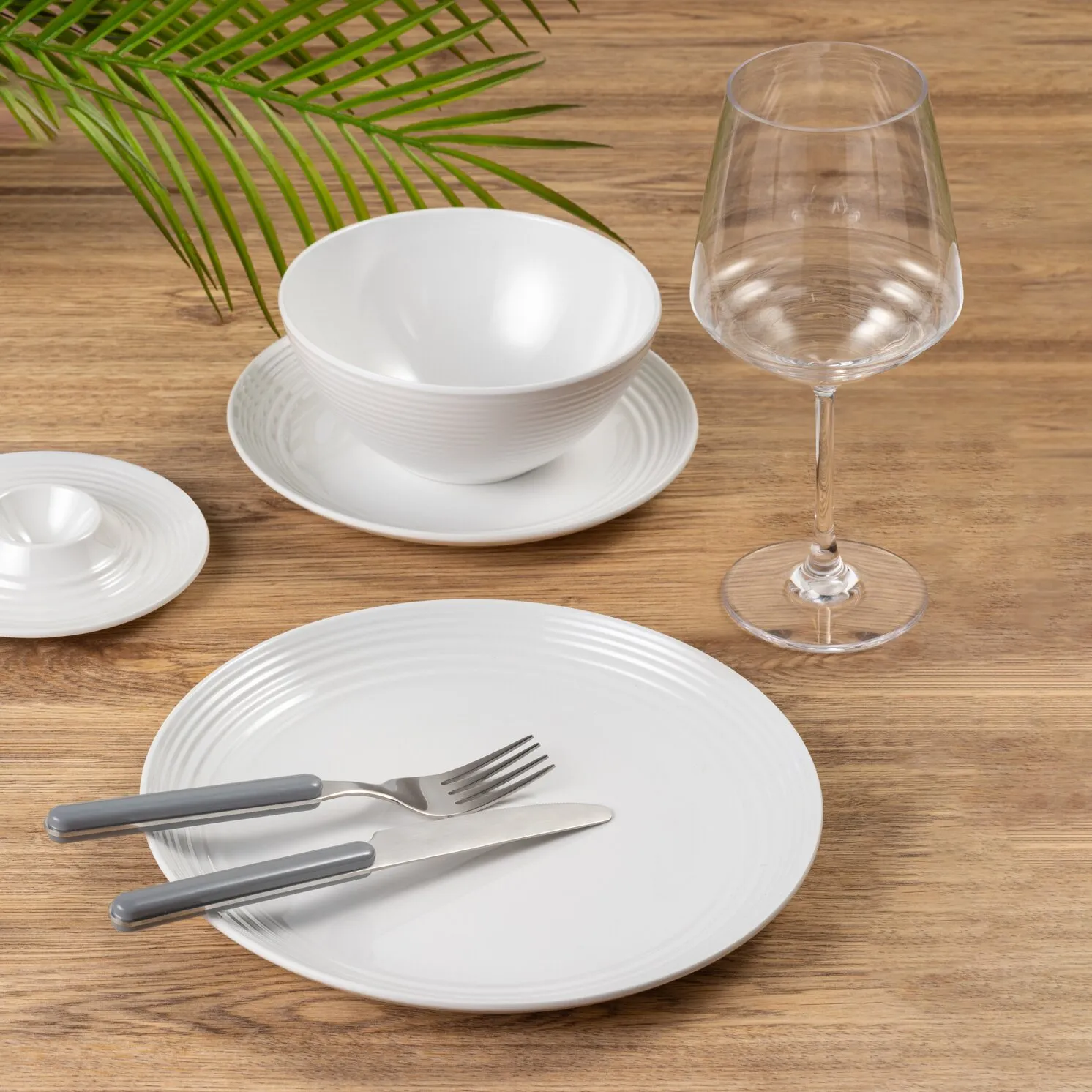 Transparentes Weinglas Spherica mit bauchiger Kelchform, langem Stiel und rundem Fuß neben weißem Geschirr auf einem Holztisch