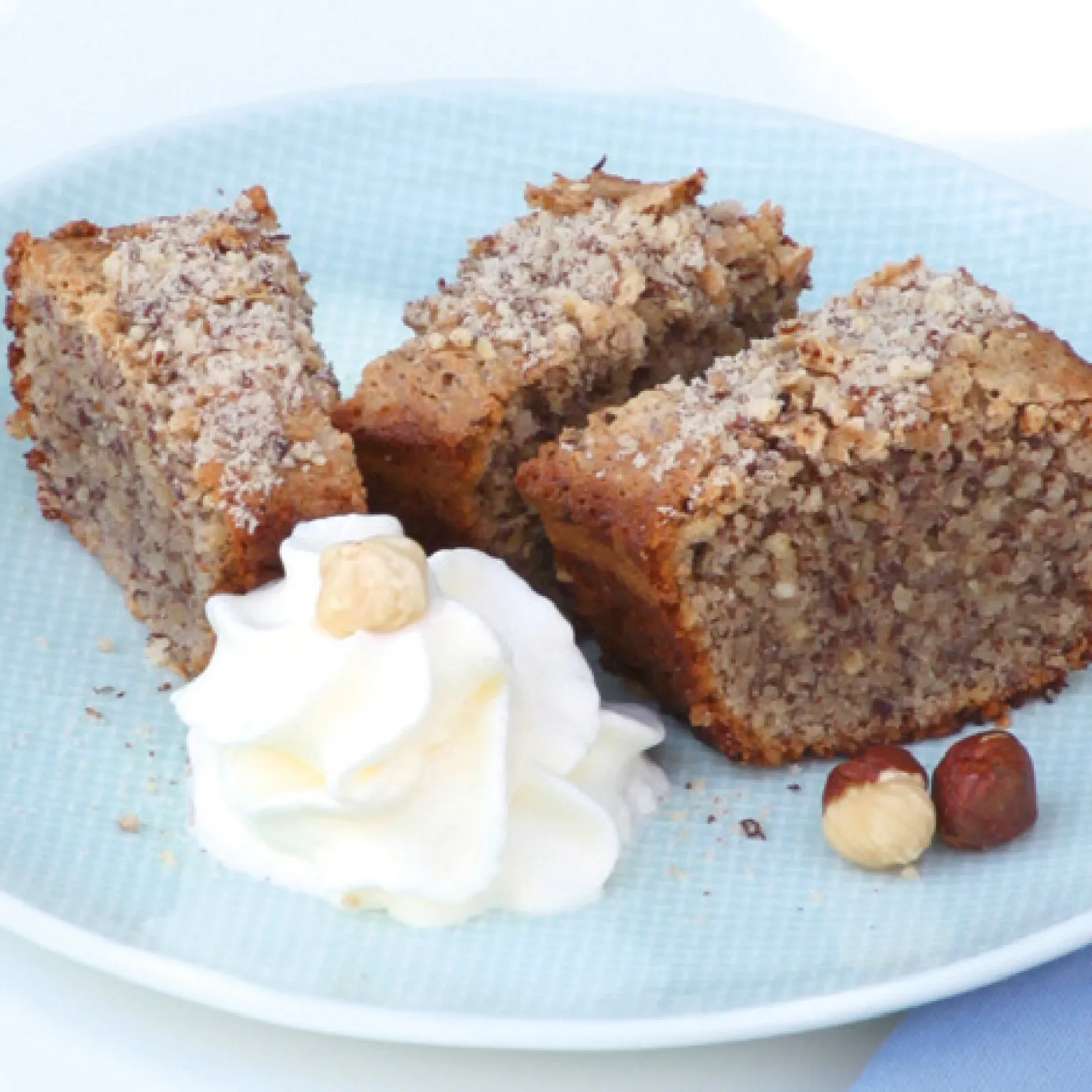 Nusskuchenstücke mit Streuseln und Puderzucker, serviert mit Sahne und Haselnüssen aus dem Omnia-Backofen-Kochbuch