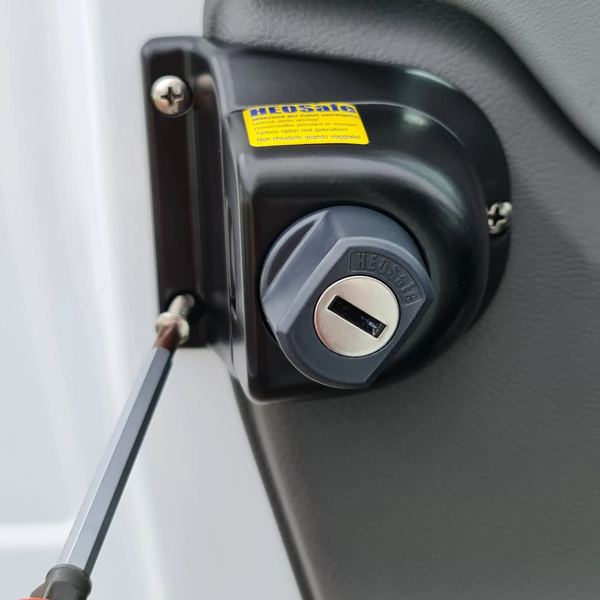 Detailansicht eines Diebstahlschutzschlosses an der Fahrertür des Ford Transit Gen7, schwarzes Gehäuse runder Zylinder gelber Warnaufkleber