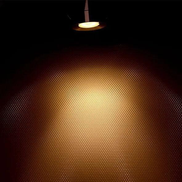 Mini-Aufbau-Spot LED1x1S22SD mit warmweißem Lichtkegel auf einer fein strukturierten Oberfläche in Nahaufnahme