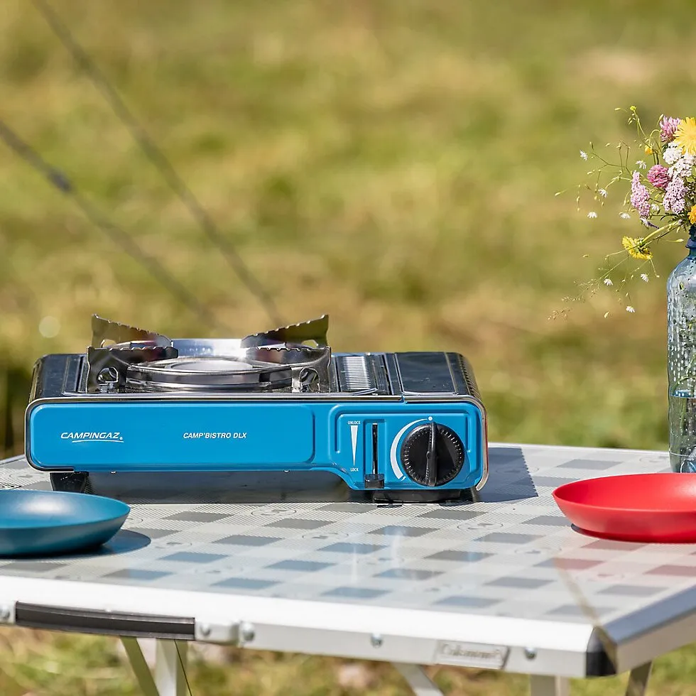 Blauer Campingaz Camp’Bistro DLX Gaskocher mit Topfauflage und Drehregler auf einem gedeckten Campingtischarsuaq