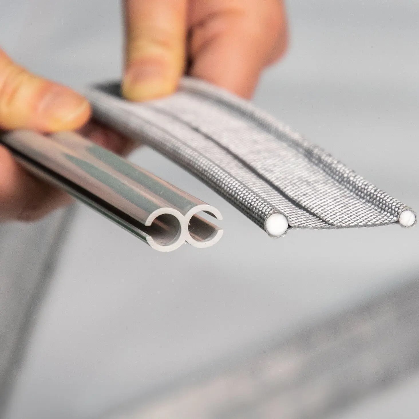 Nahaufnahme von zwei gebogenen weißen Kunststoffrohren und zwei silbernen geflochtenen Metallstangen mit weißen Endkappen, die von einer Hand gehalten werden