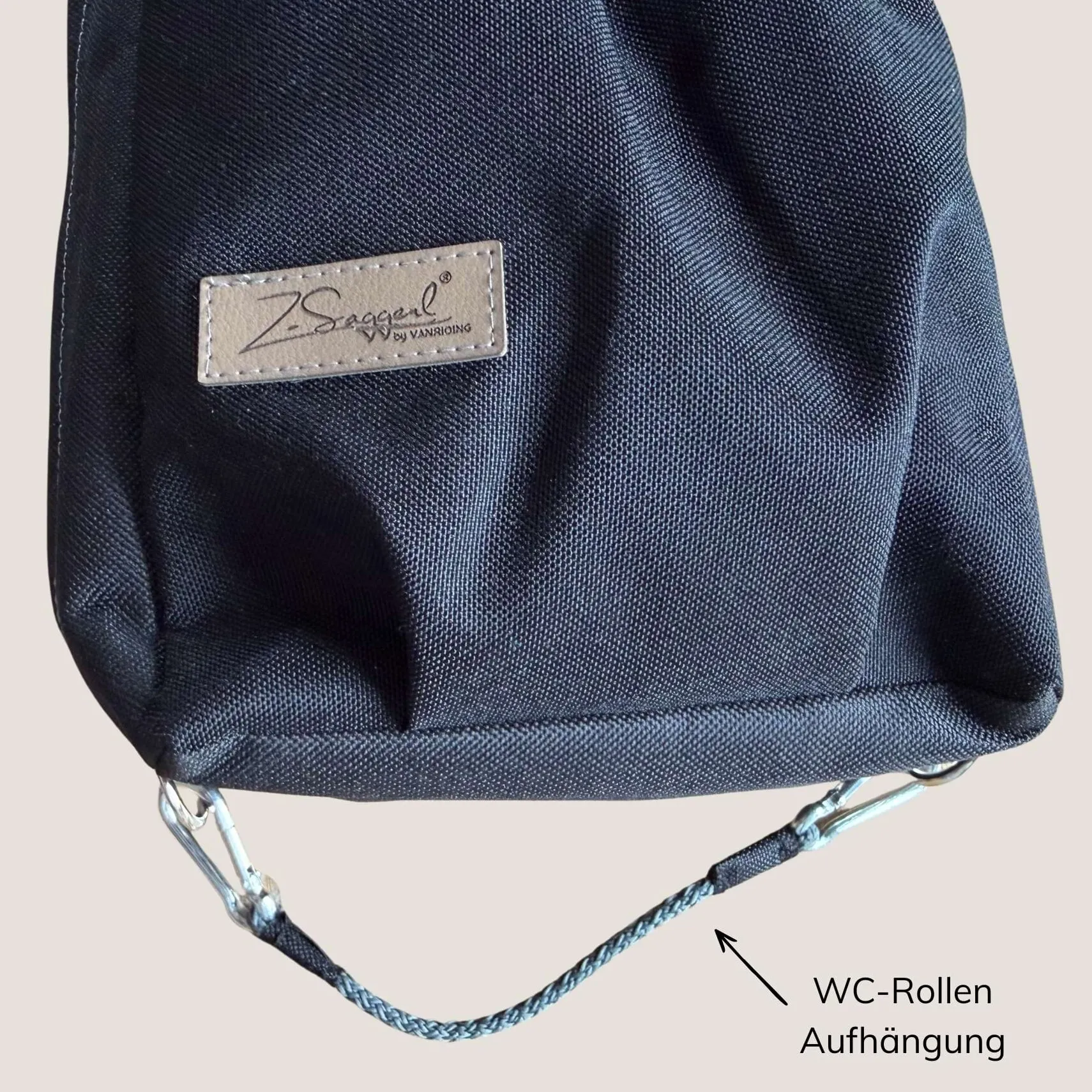 Nahaufnahme eines dunkelblauen Canvas-Stoffbeutels mit hellem Lederetikett und Logo-Aufdruck; sichtbare weiße Naht und Tragriemen mit Metallbeschlägen