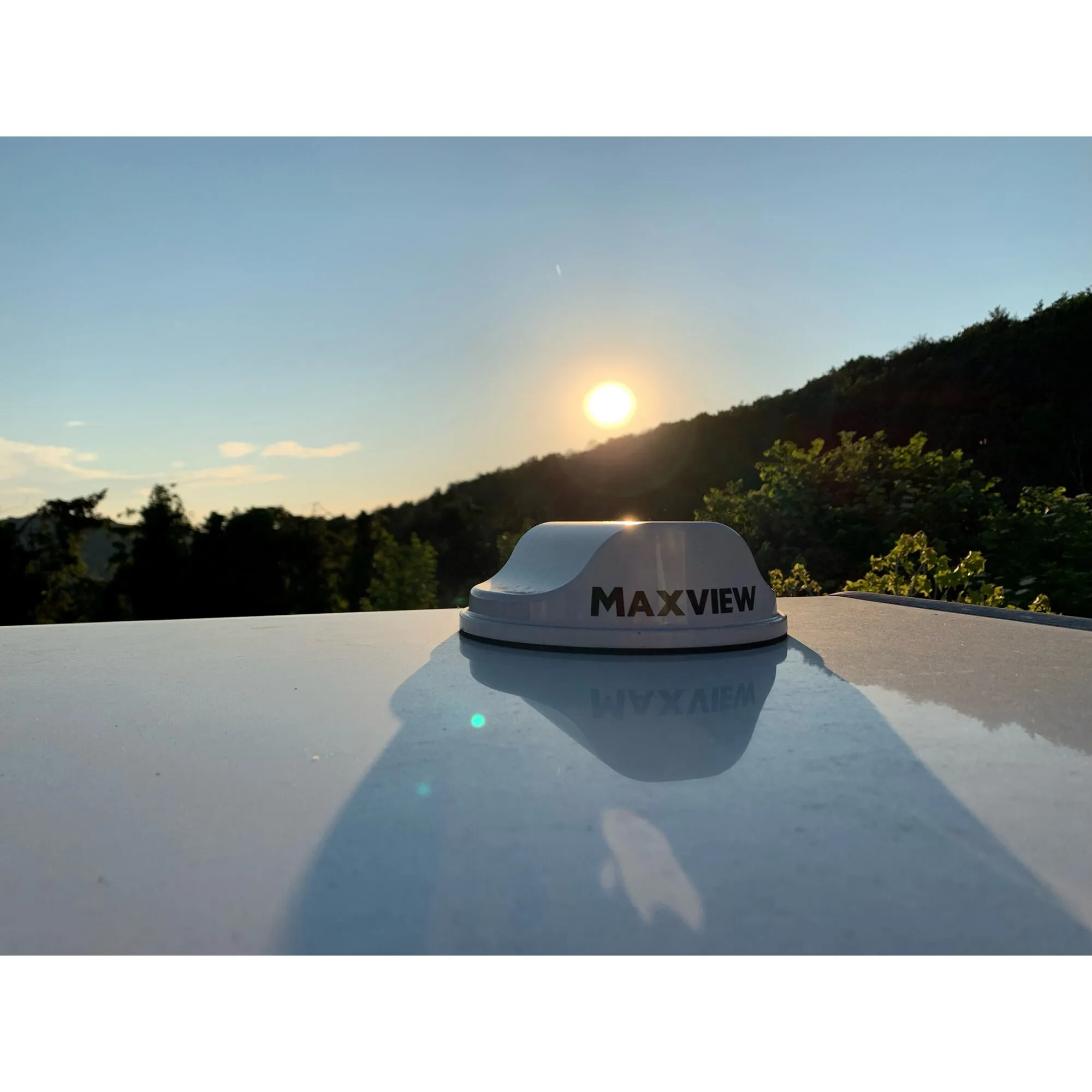 Maxview Roam 5G Routerset mit anthrazitfarbenem Sockel auf einem Fahrzeugdach vor bewaldeter Landschaft im Sonnenuntergang