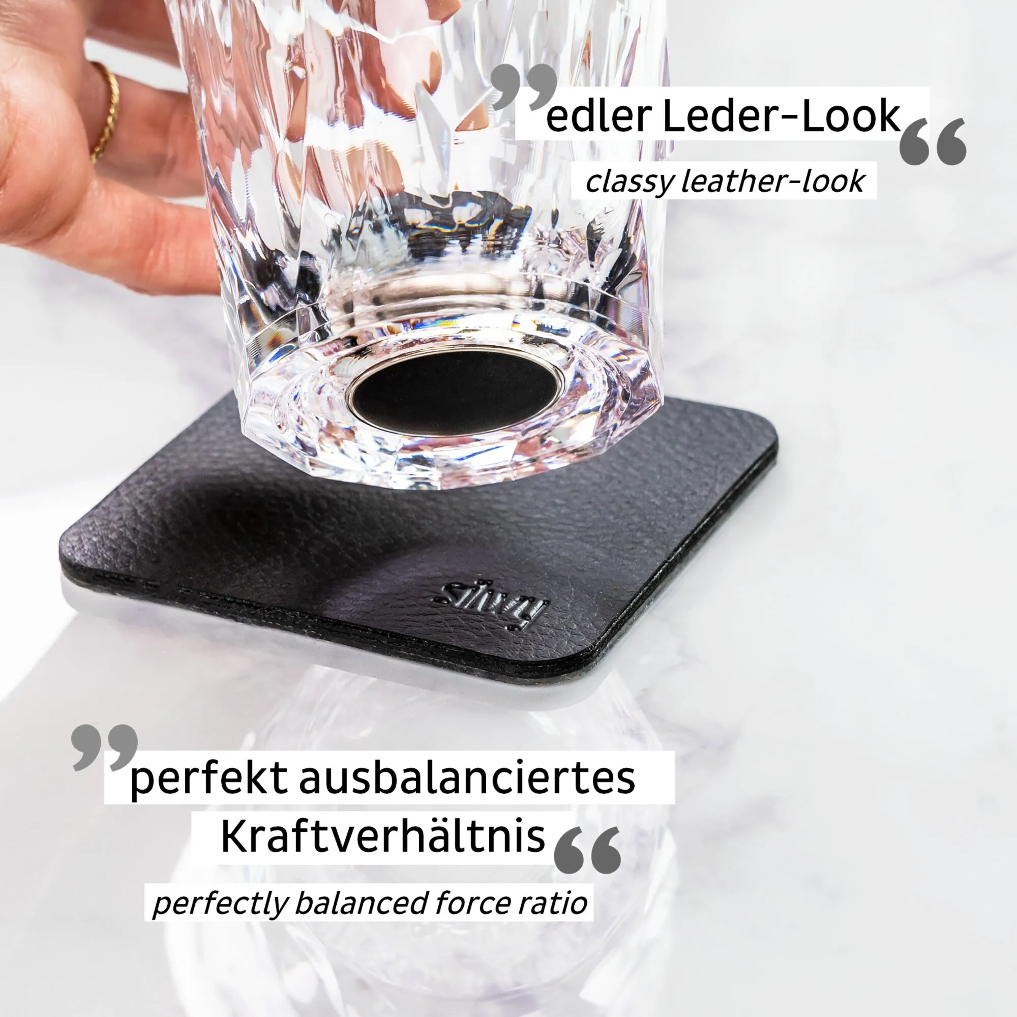 Transparentes, facettiertes Magnet-Kunststoffglas für Longdrinks mit schwarzem Magnetboden auf einer schwarzen Unterlage in einer Hand