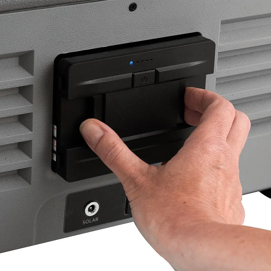 Hand setzt schwarzen Akku an der Rückseite einer grauen Kühlbox ein; Sichtbar sind Powerknopf und LED-Indikatoren, Solaranschluss unten links